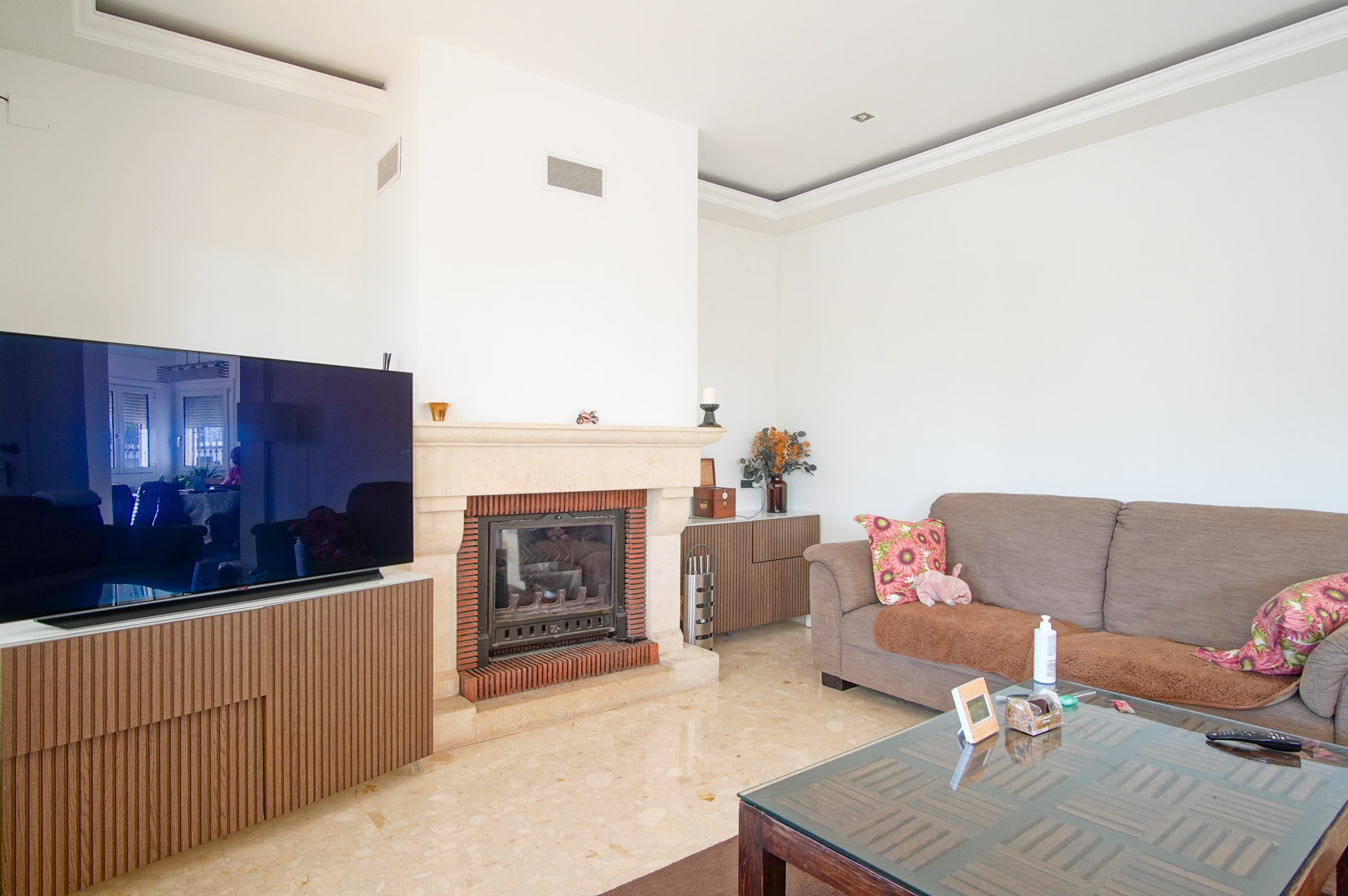 Lichte woonkamer met een stenen open haard met bakstenen details, gepolijste marmeren vloer en houten kastenwand voor de televisie.
