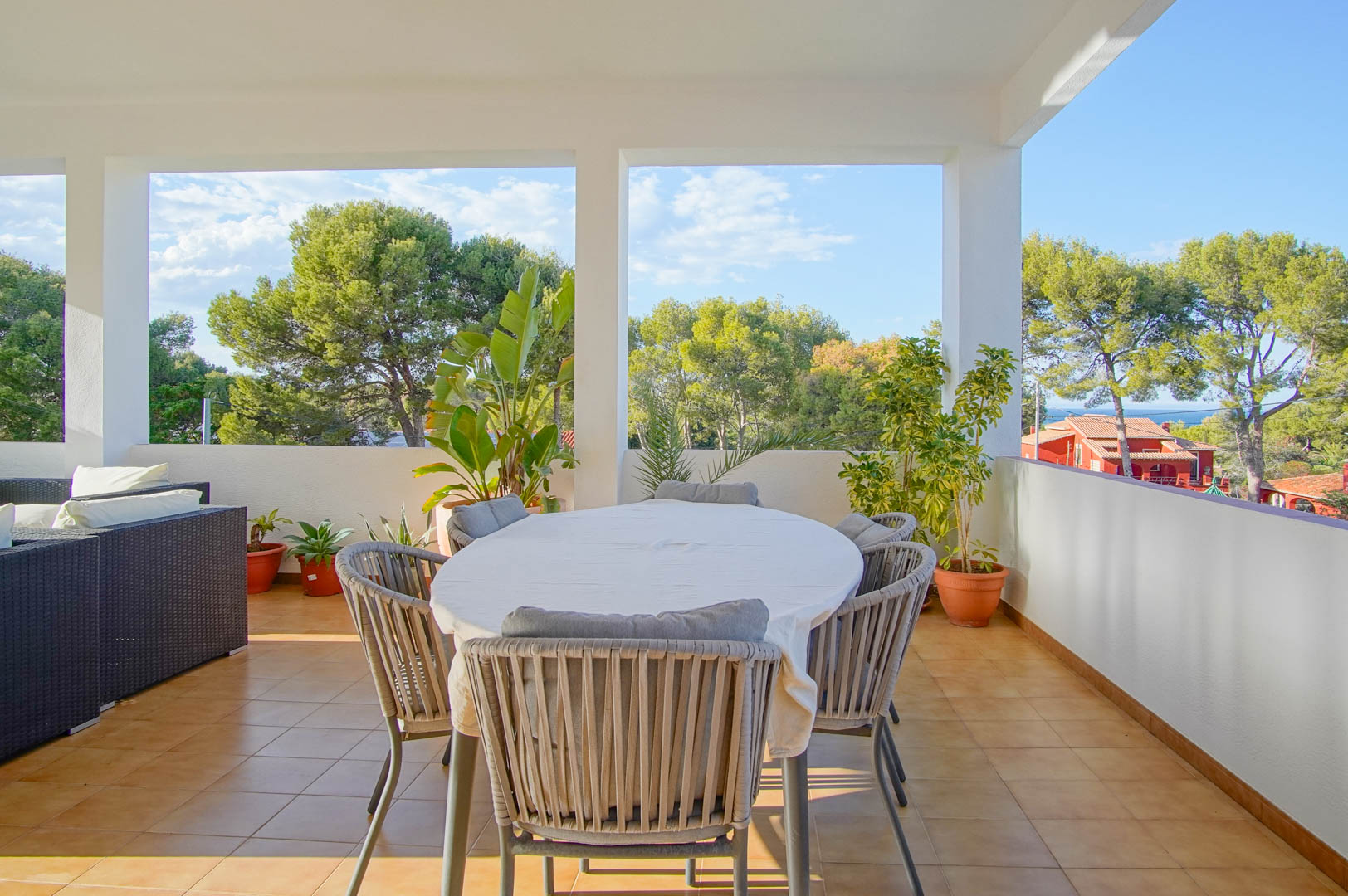 Overdekt terras met een eethoek en loungeset, met vrij uitzicht op het mediterrane dennenbos en de verre zeehorizon in de wijk Las Rotas.