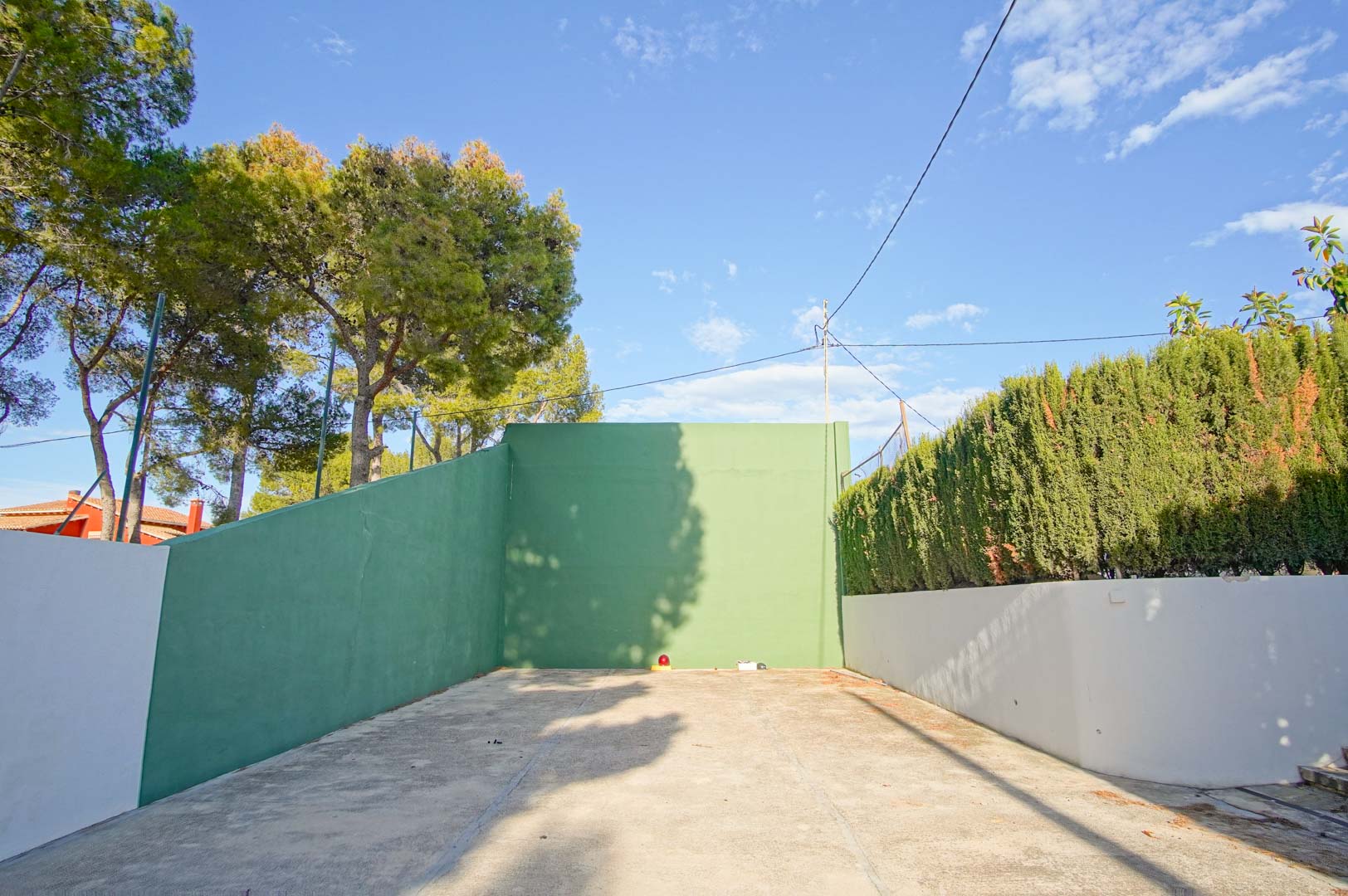 Privé frontonbaan met groene muren en een betonnen vloer, omgeven door volwassen pijnbomen en hoge hagen voor maximale privacy.