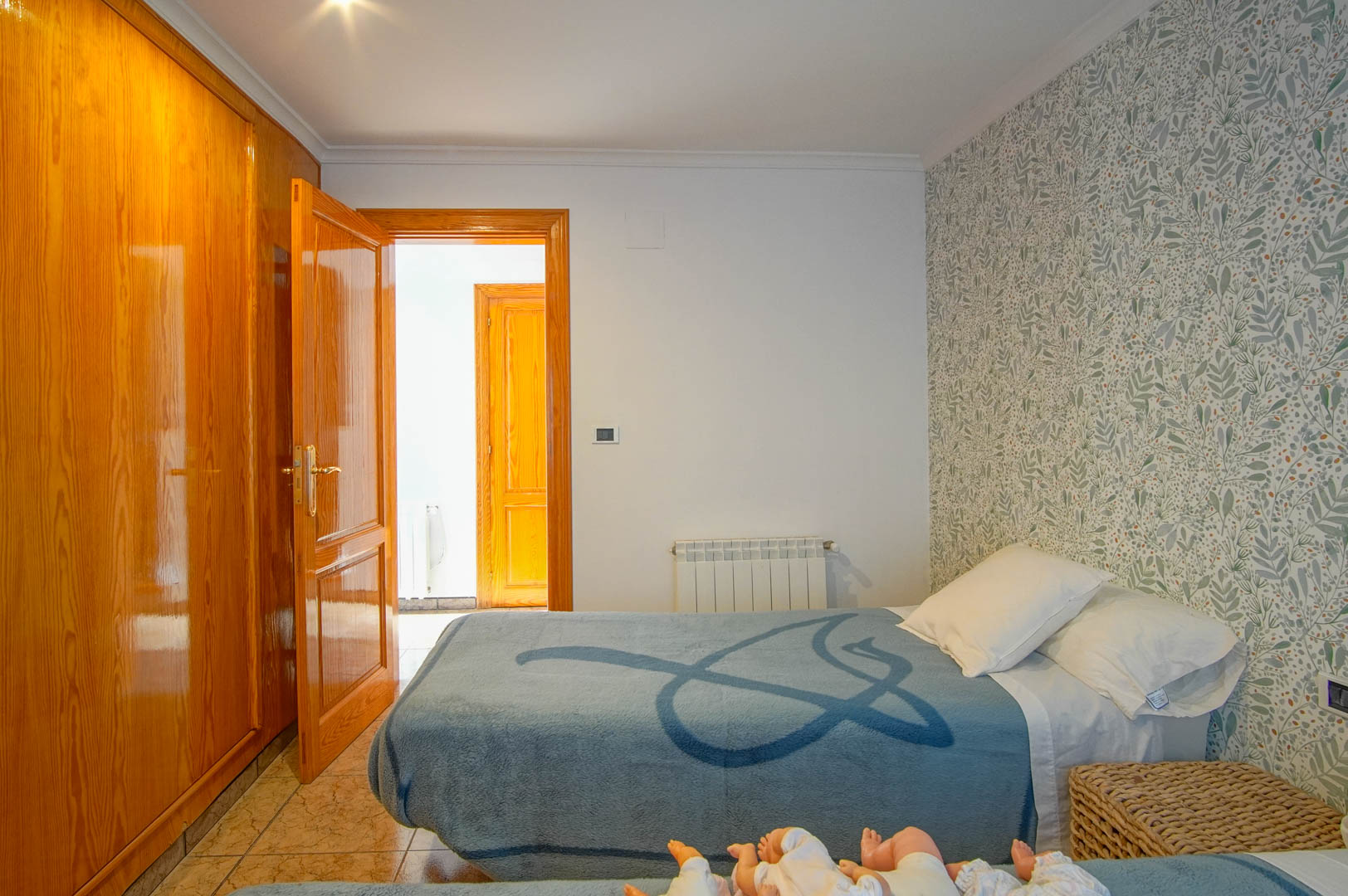 Slaapkamer met een gepolijste houten inbouwkast, botanisch behang, een tegelvloer en een aan de muur gemonteerde radiator.