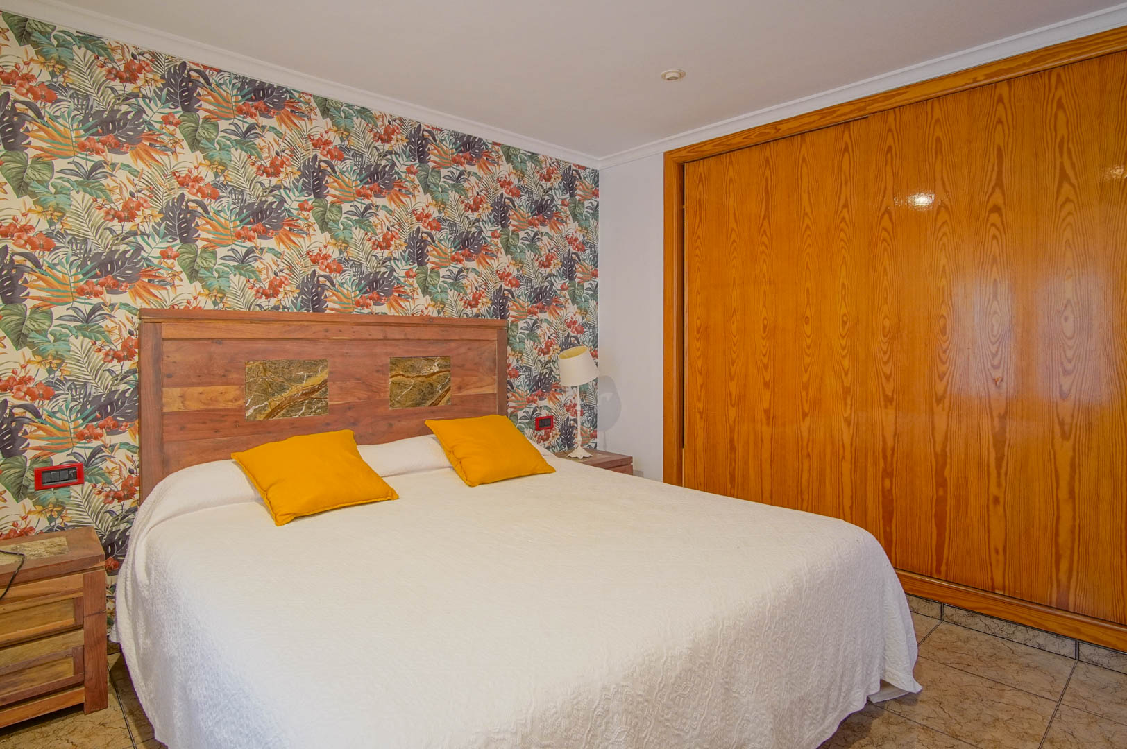 Slaapkamer met tropisch behang, een houten hoofdbord met natuurstenen details en een ruime ingebouwde houten kledingkast.