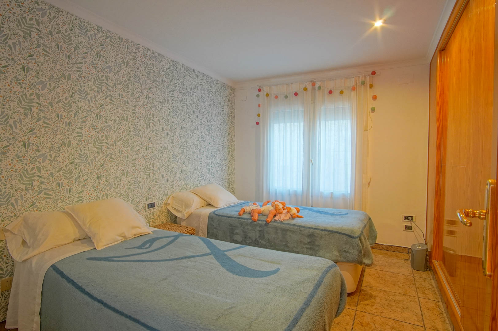 Slaapkamer met twee eenpersoonsbedden, botanisch behang, ingebouwde houten kastenwand en een onderhoudsvriendelijke tegelvloer.