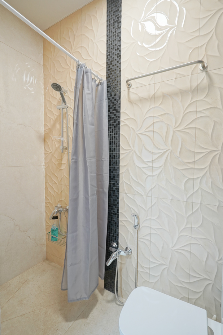 Badkamer met crèmekleurige reliëfwandtegels, een verticale zwarte mozaïekstrip en chromen kranen inclusief handdouche.