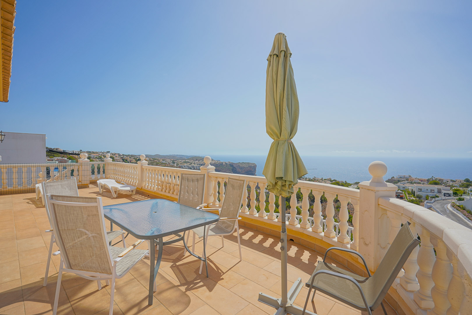 Bovenste terras met glazen eettafel, buitenstoelen en witte balustrade, met panoramisch uitzicht over de Middellandse Zee en de kliffen.