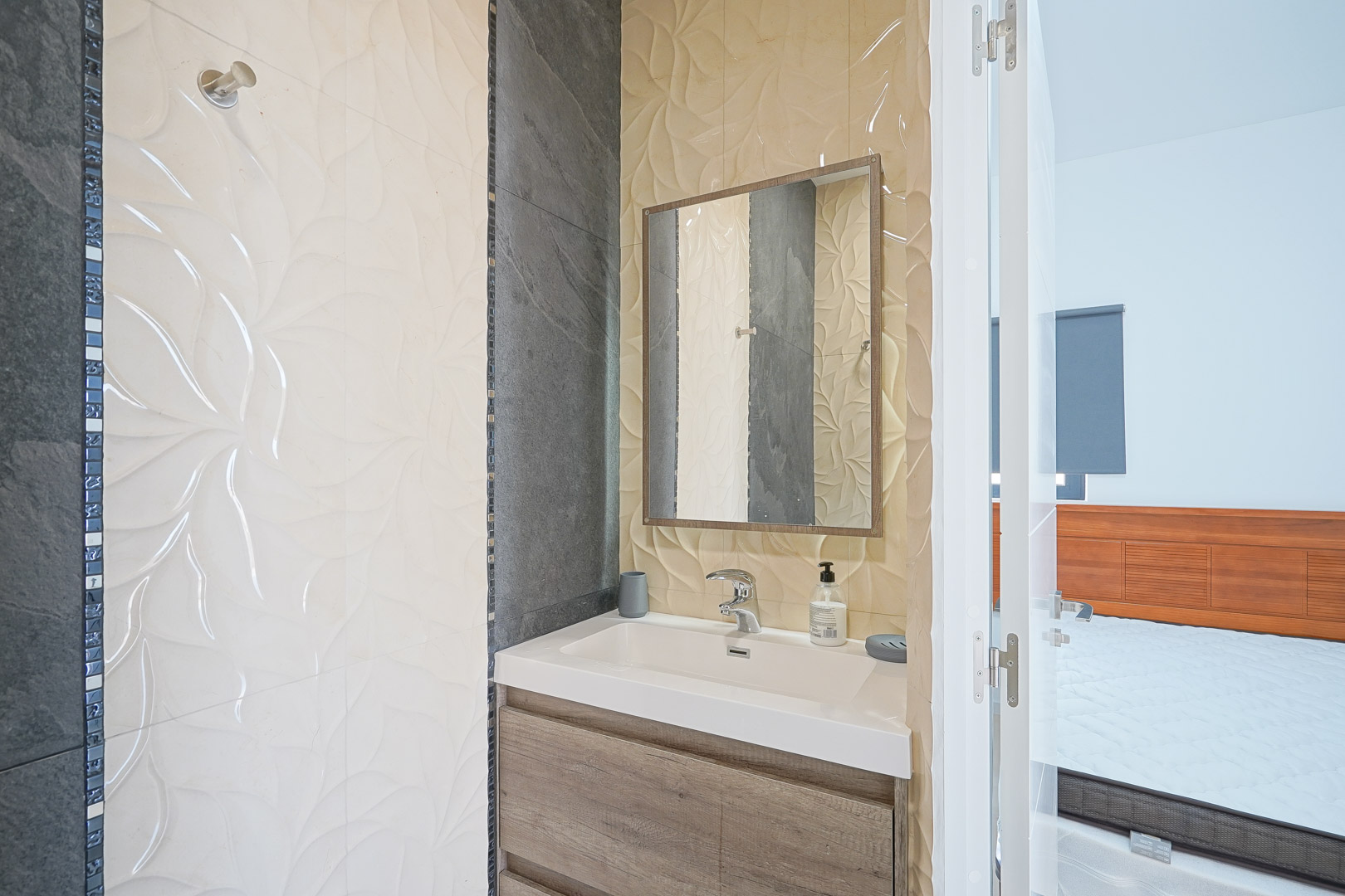 Ensuite badkamer met houten wastafelmeubel, geïntegreerde wasbak en decoratieve wandtegels met reliëf en donkere accenten.
