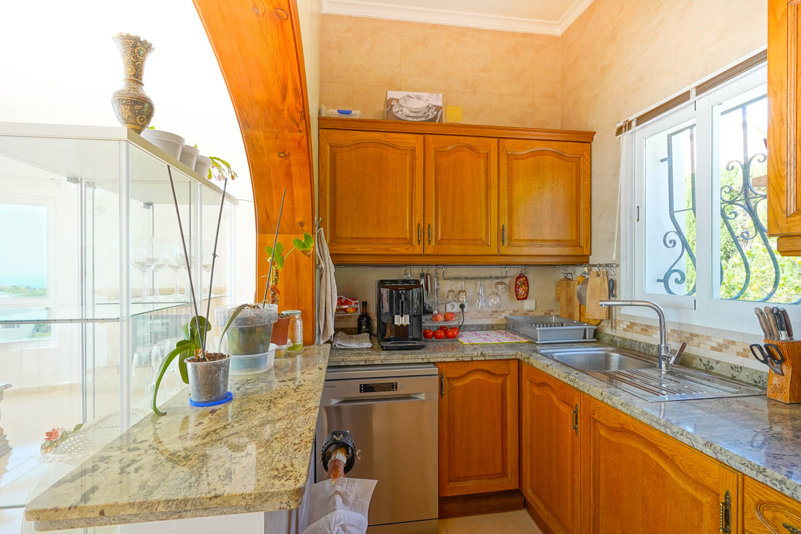 Halfopen keuken met klassieke houten kasten, granieten werkbladen en rvs-apparatuur, sfeervol omlijst door een robuuste massief houten boogconstructie.