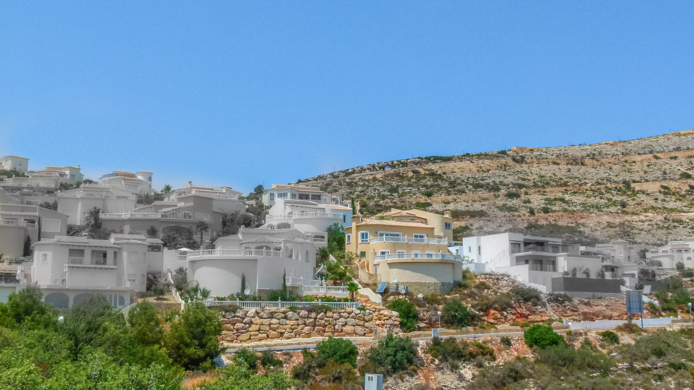 Panoramisch uitzicht op trapsgewijs gebouwde witte villa's op de helling van Cumbre del Sol, met natuurstenen muren en gebogen terrassen.