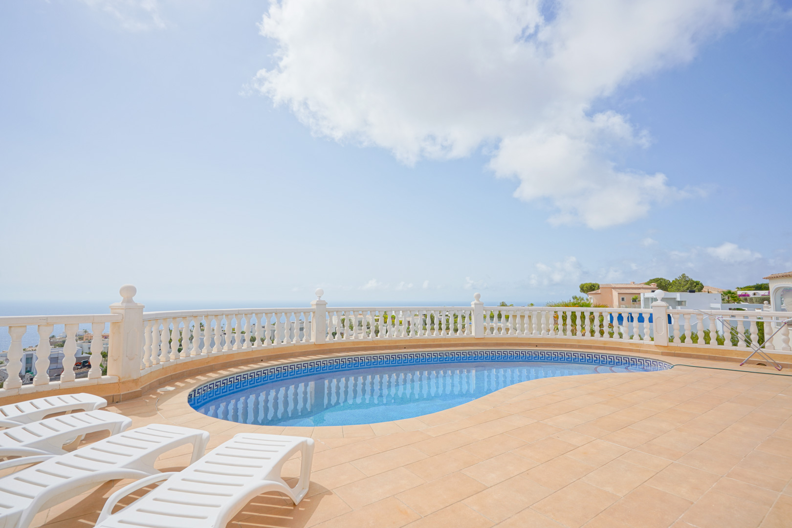 Terras met niervormig zwembad, witte balustrade en panoramisch uitzicht op de Middellandse Zee, voorzien van ligbedden op terracotta tegels.