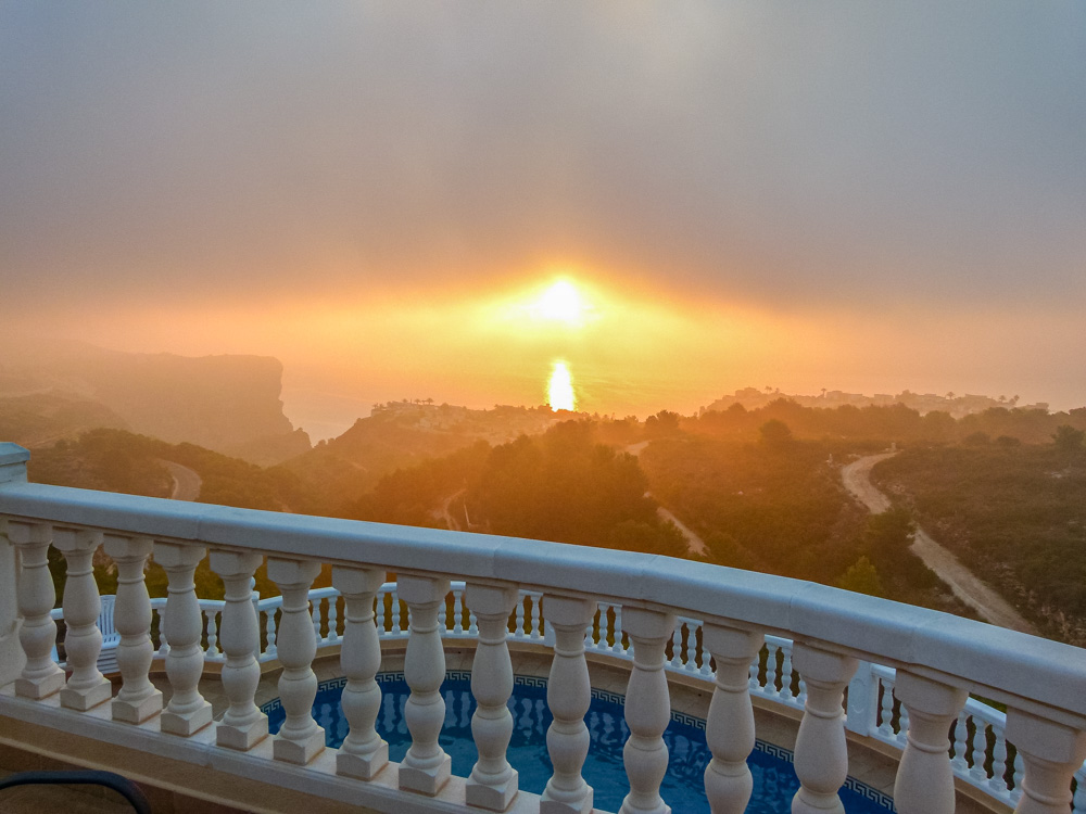 Uitzicht vanaf het terras met witte balustrade op het zwembad en de zonsondergang boven de kliffen van de Middellandse Zee.
