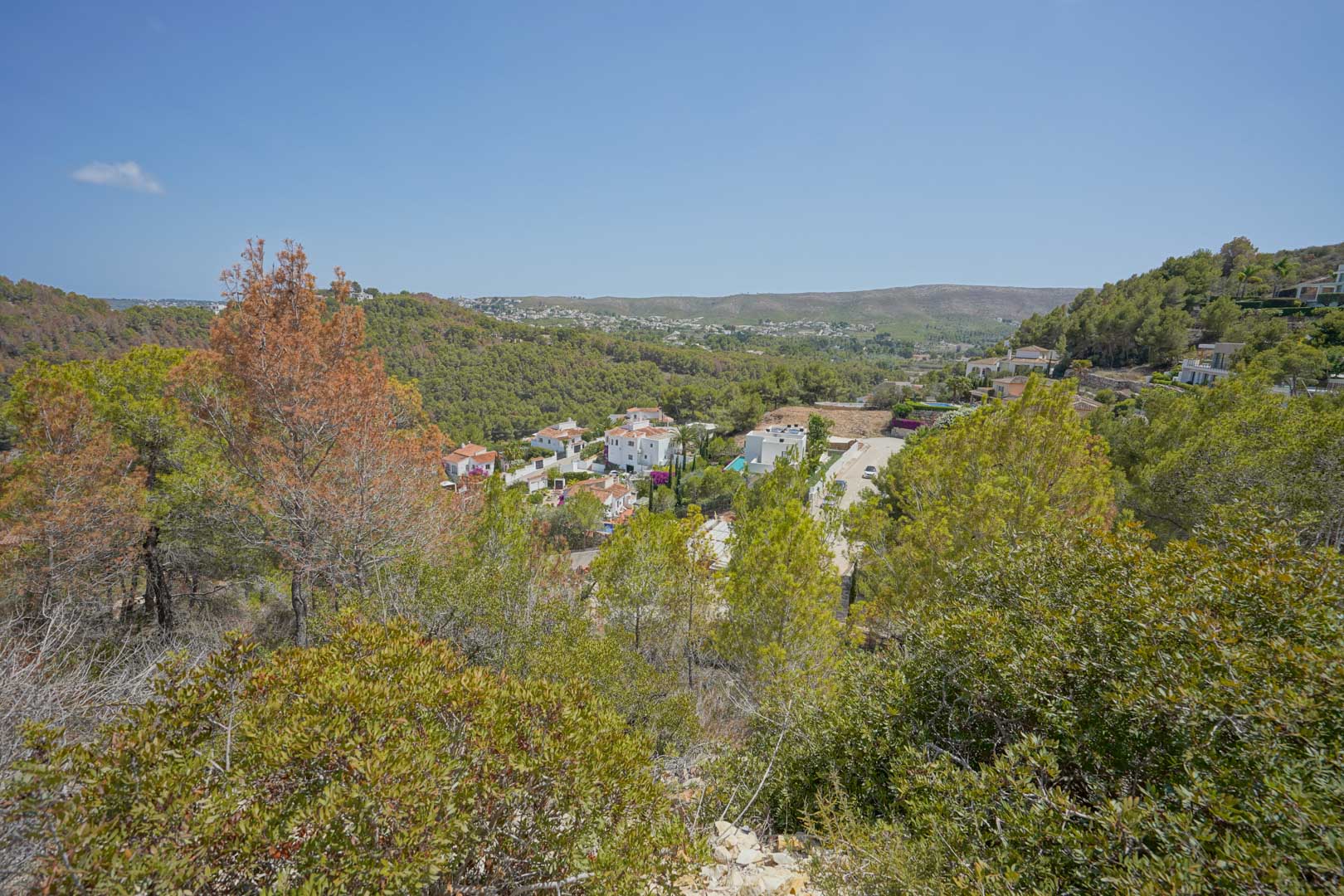 Verhoogd panoramisch uitzicht vanaf het perceel over een groene vallei met witte villa's en de omliggende mediterrane heuvels.