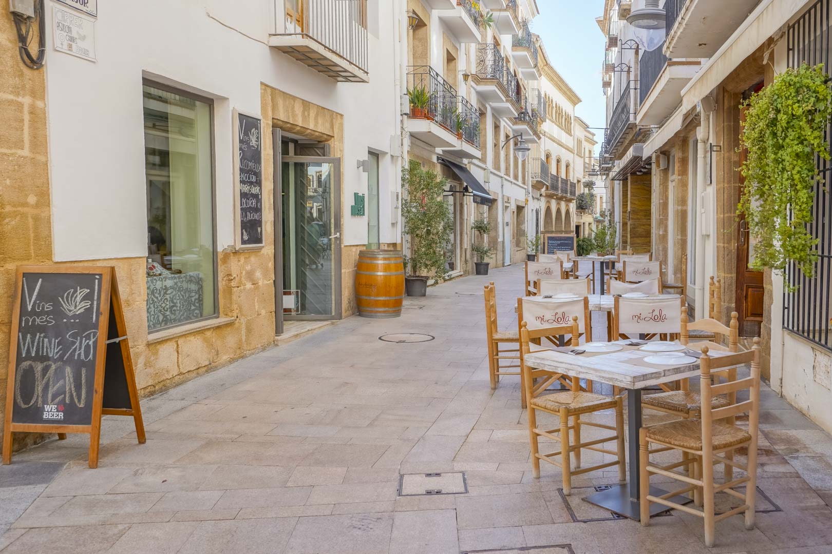 Voetgangersstraat met traditionele stenen gevels, terrassen van restaurants en lokale winkels in een verzorgde mediterrane stedelijke omgeving.