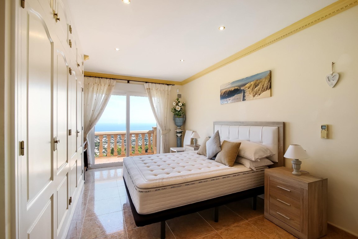 Hoofdslaapkamer met kamerhoge inbouwkasten en glazen schuifdeuren die toegang bieden tot een terras met uitzicht op zee.