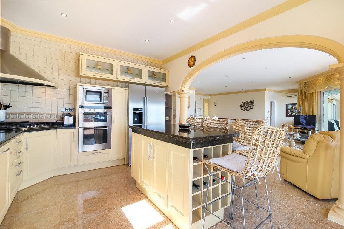 Open keuken met een donker granieten kookeiland, rvs-apparatuur en een karakteristieke boogverbinding naar de aangrenzende woonkamer.