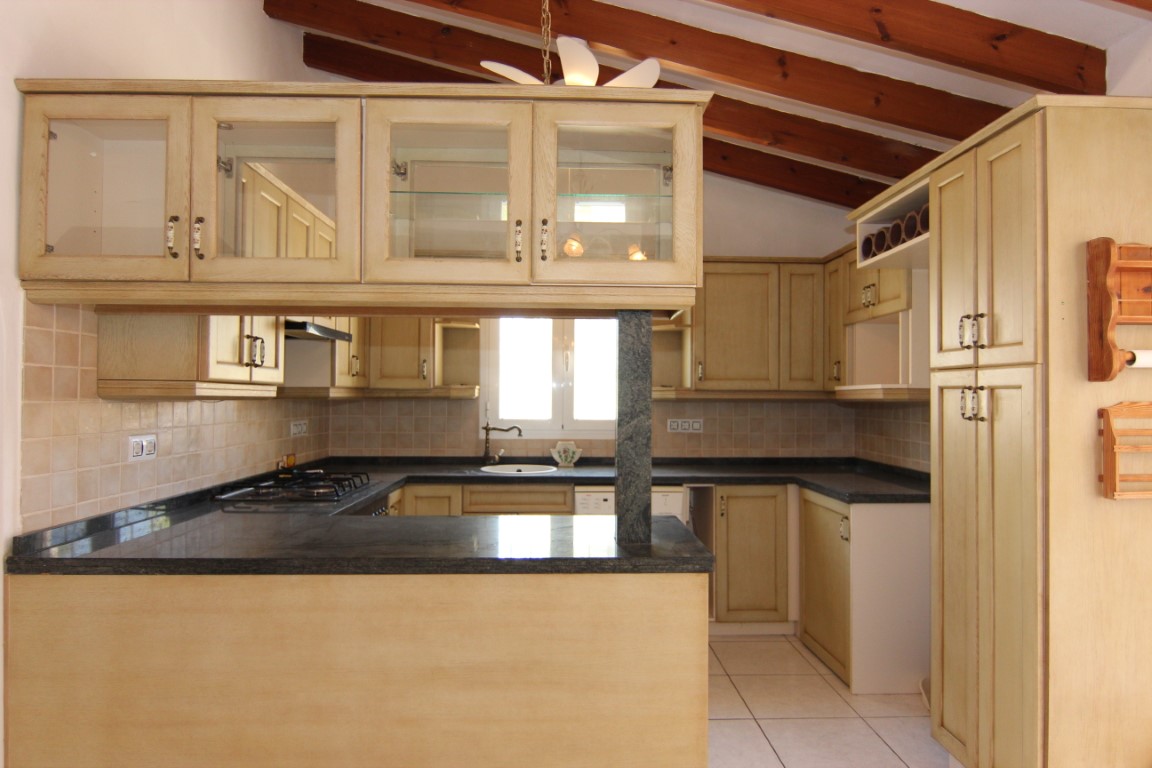Rustieke keuken met houten plafondbalken, donkere granieten werkbladen en crèmekleurige kasten met vitrines en een functionele ontbijtbar.