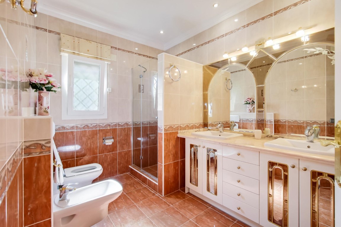 Volledige badkamer met dubbele wastafel, boogvormige spiegels met geïntegreerde verlichting en een glazen inloopdouche.
