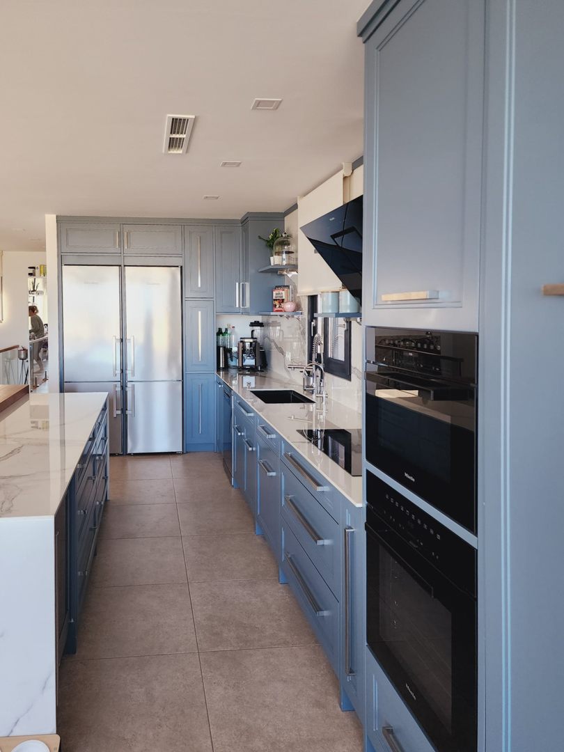 Designkeuken met blauwgrijze kasten, marmerlook werkbladen en geïntegreerde Miele-apparatuur, inclusief dubbele ovens en een grote roestvrijstalen koelkast.