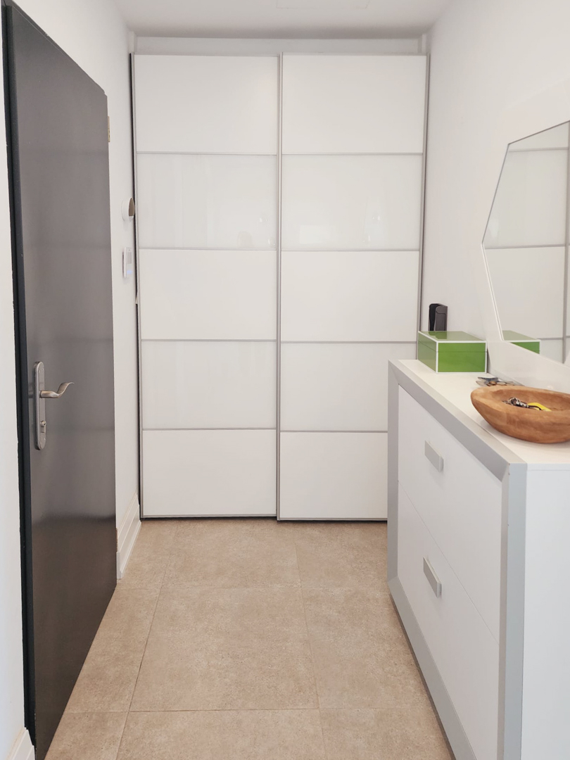 Hal met een witte inbouwkast met schuifdeuren, een strak dressoir en een neutrale tegelvloer in zandkleur.