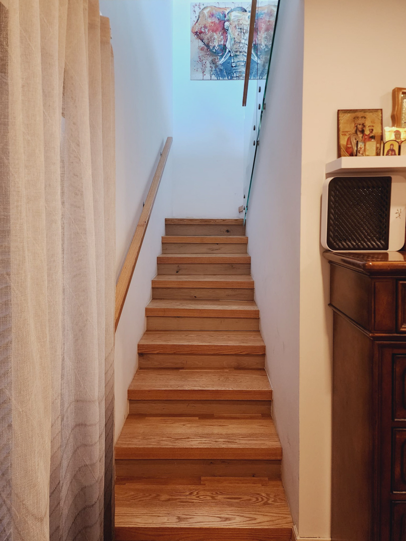 Interne houten trap met bijpassende leuning en glazen balustrade, verlicht door natuurlijk licht van boven en voorzien van decoratieve wandkunst.