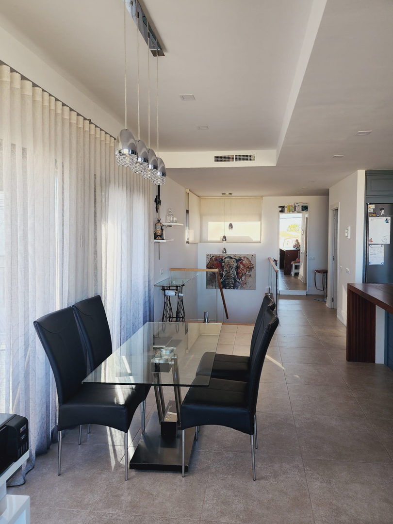 Lichte eethoek met glazen tafel, zwarte lederen stoelen en moderne hanglampen, gelegen naast grote ramen en de trap met glazen balustrade.