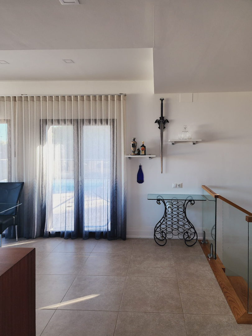 Lichte woonruimte met porseleinen tegelvloer, een decoratieve glazen consoletafel en een moderne trap met glazen balustrade en houten afwerking.