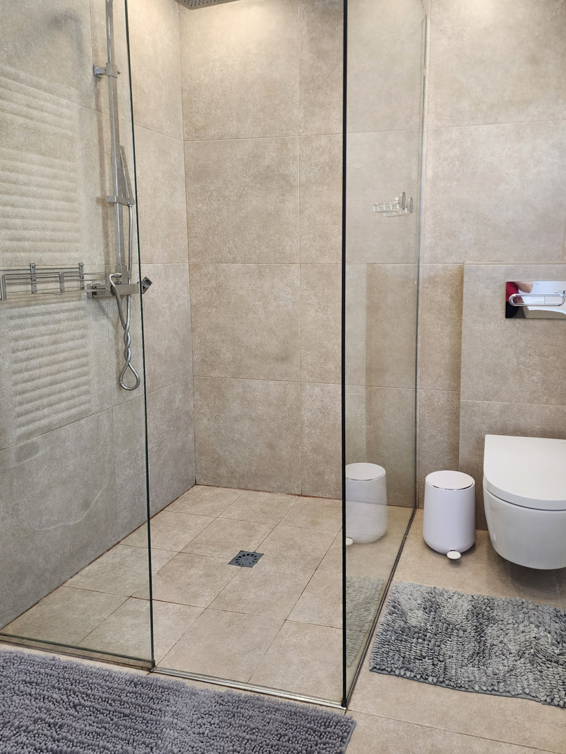 Moderne badkamer met inloopdouche, glazen wand en zandkleurige porseleinen tegels. Voorzien van een hangend toilet en chromen kranen.