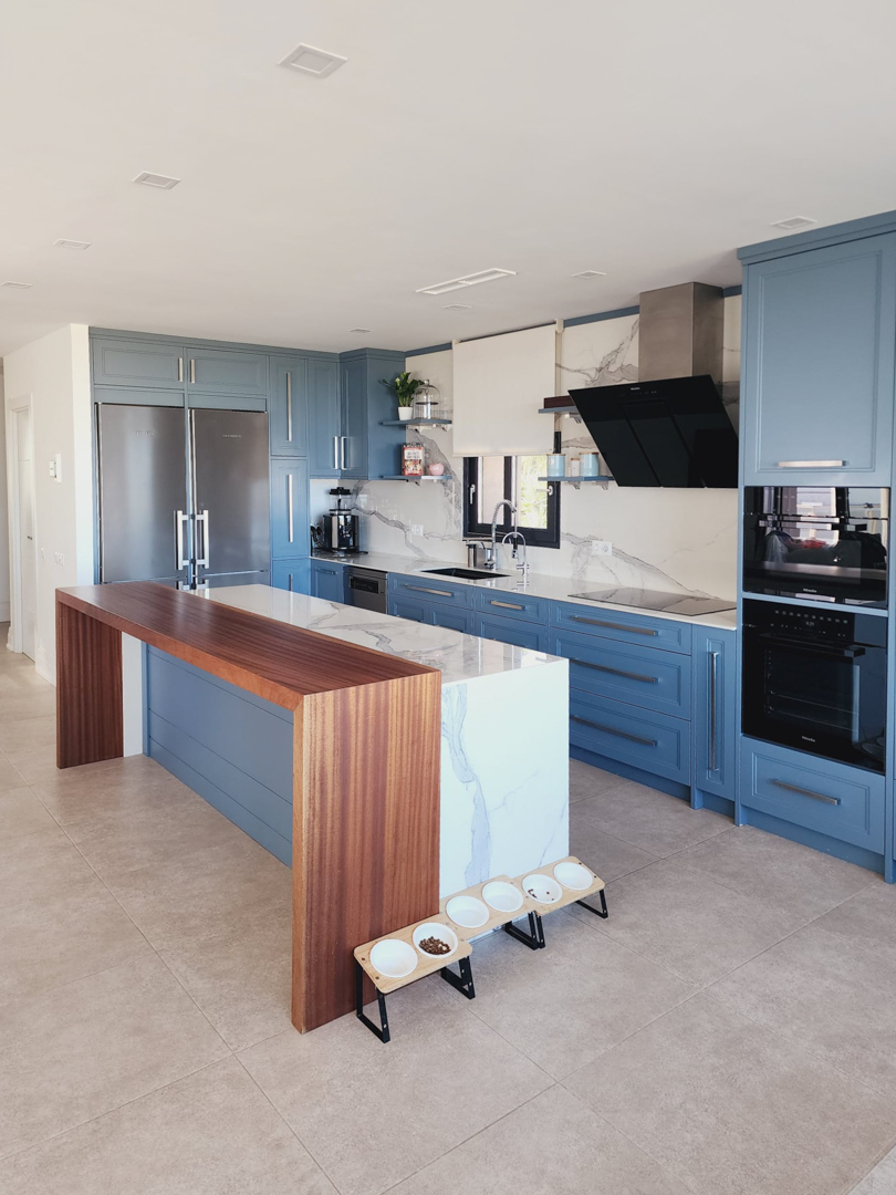 Moderne keuken met blauwe kasten, een marmeren kookeiland met geïntegreerde houten bar en hoogwaardige Miele-apparatuur tegen een bijpassende achterwand.