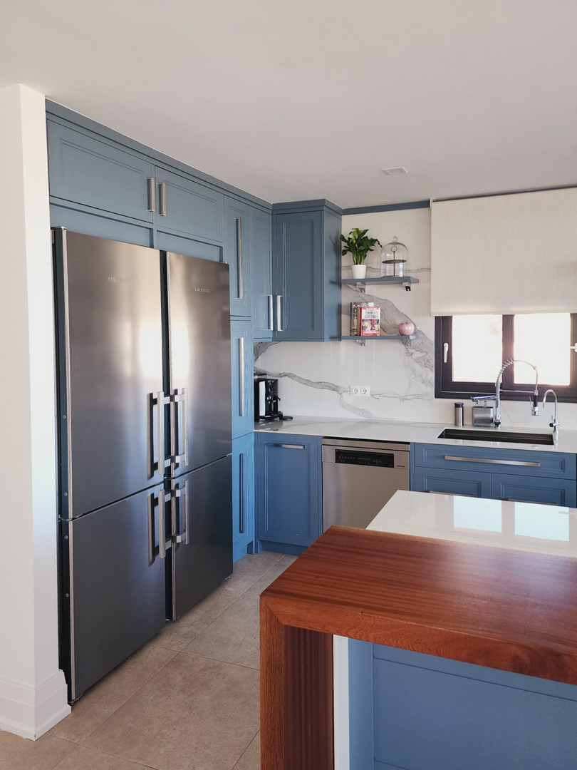 Moderne keuken met blauwe kasten, marmerlook achterwand en hoogwaardige rvs-apparatuur. Een houten barblad vormt een warm contrast met het witte werkblad.