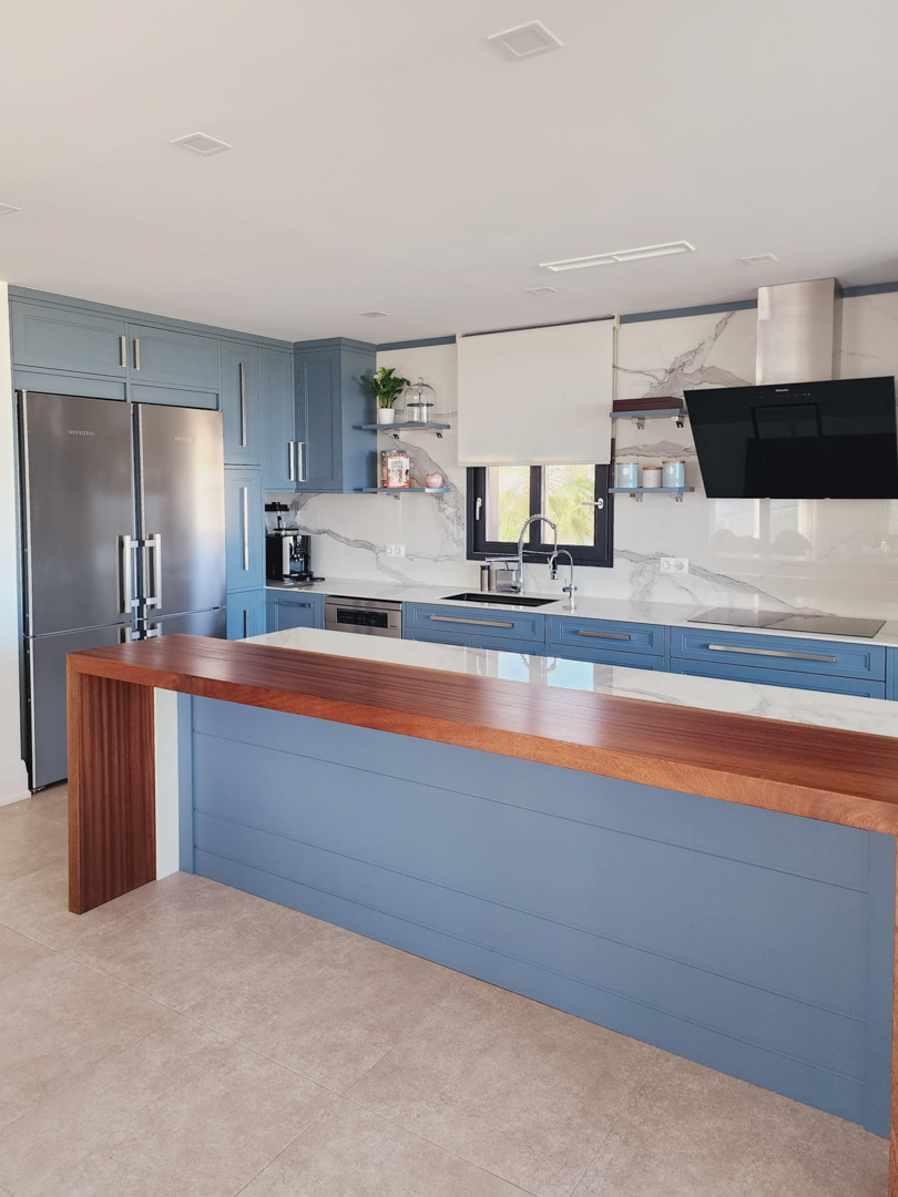 Moderne keuken met blauwe kasten, marmerlook werkbladen en een massief houten bar. Voorzien van inbouwapparatuur en een ruime, lichte werkplek.