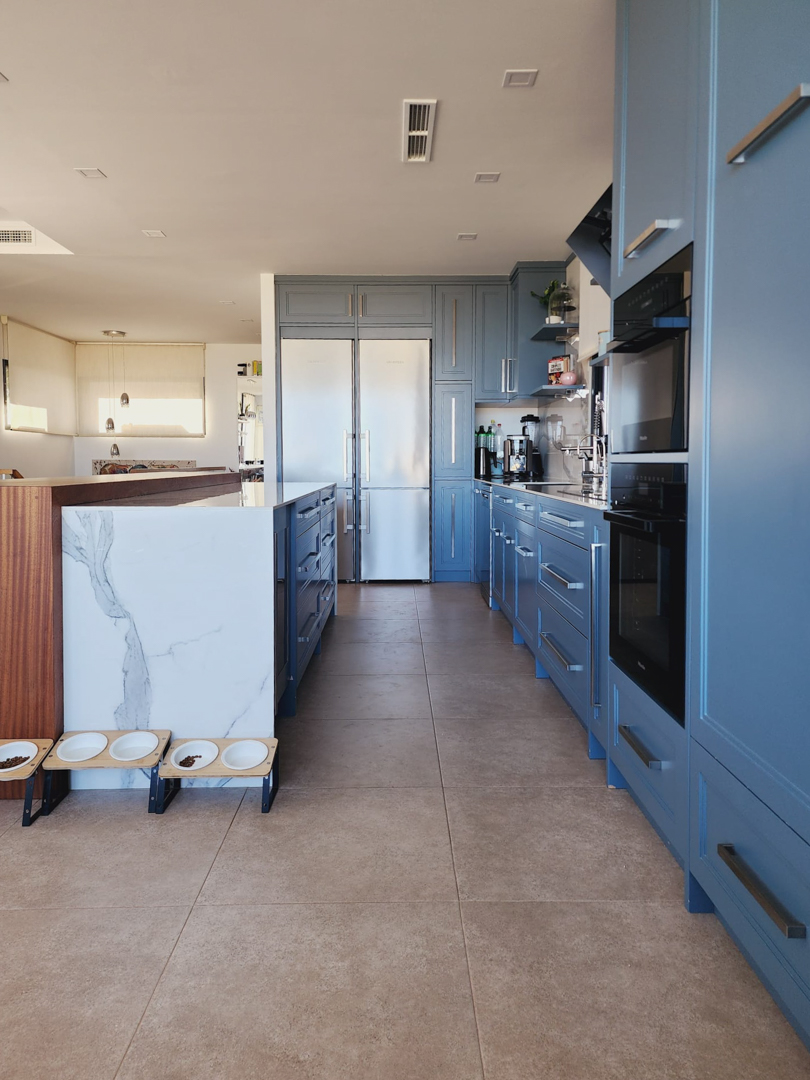 Moderne keuken met pastelblauwe kasten, een marmeren kookeiland en geïntegreerde Miele-apparatuur. Voorzien van een keramische tegelvloer en inbouwverlichting.