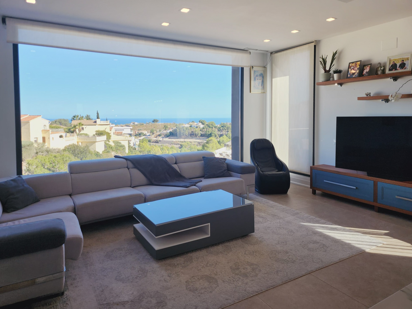 Moderne woonkamer met een groot panoramisch raam met uitzicht op zee, een grijze hoekbank, design salontafel en inbouwspots.
