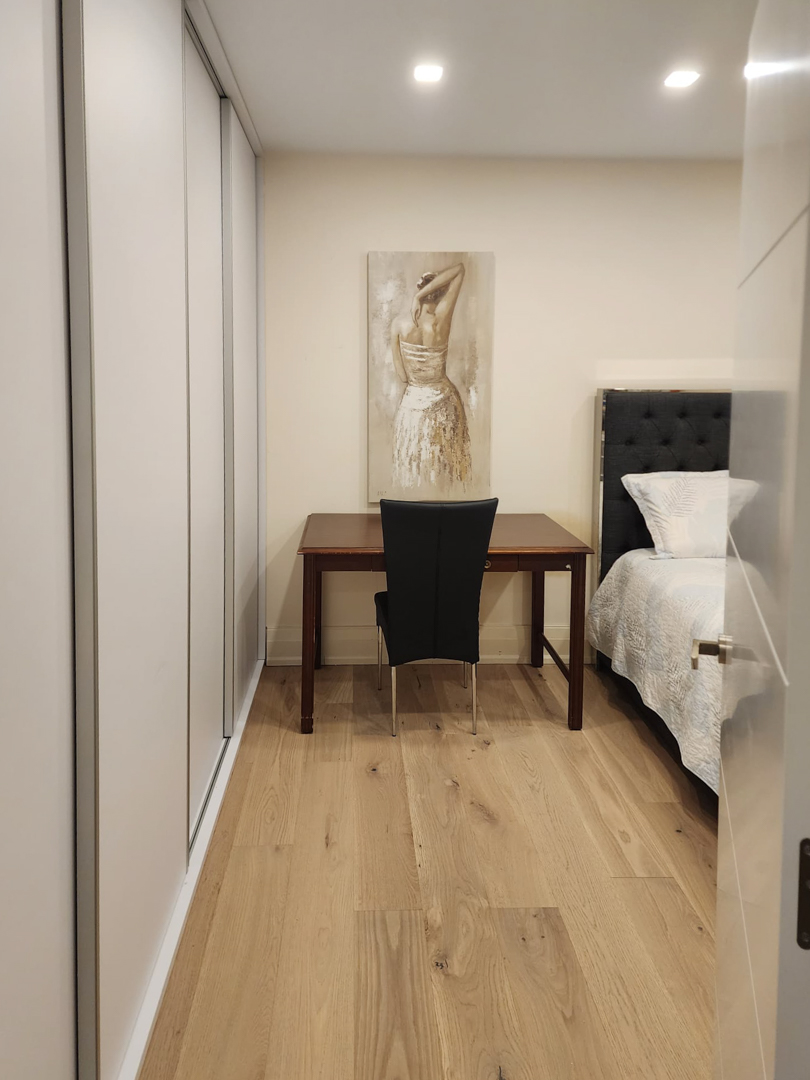 Slaapkamer met kamerhoge inbouwkasten, een houten bureau en een eikenhouten vloer verlicht door subtiele inbouwspots in het plafond.