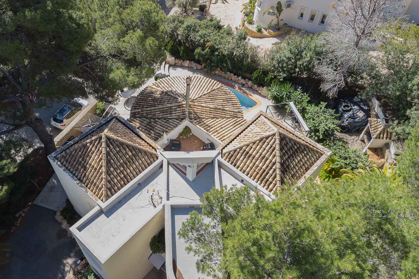 Luchtfoto van de villa met unieke piramidale pannendaken, een centrale schoorsteen en een dakterras, omgeven door volgroeide mediterrane beplanting.
