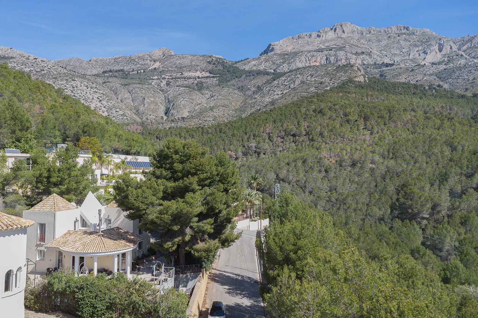 Panoramisch uitzicht op de villa midden in de natuur, met de mediterrane architectuur tegen een dicht dennenbos en de majestueuze bergketen.