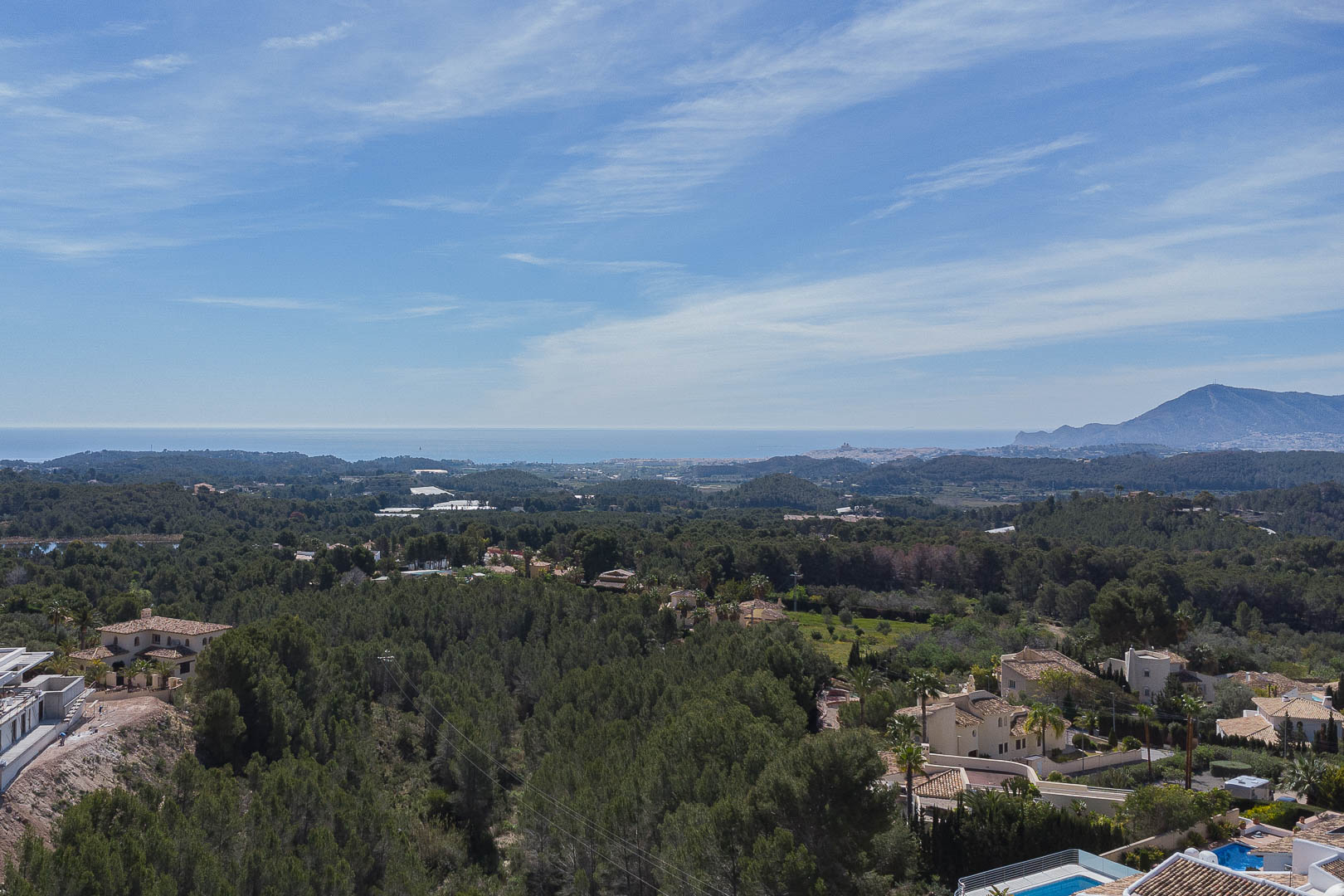 Panoramisch uitzicht vanaf het bovenste terras over een dicht dennenbos, de Middellandse Zeekust aan de horizon en bergsilhouetten onder een heldere hemel.