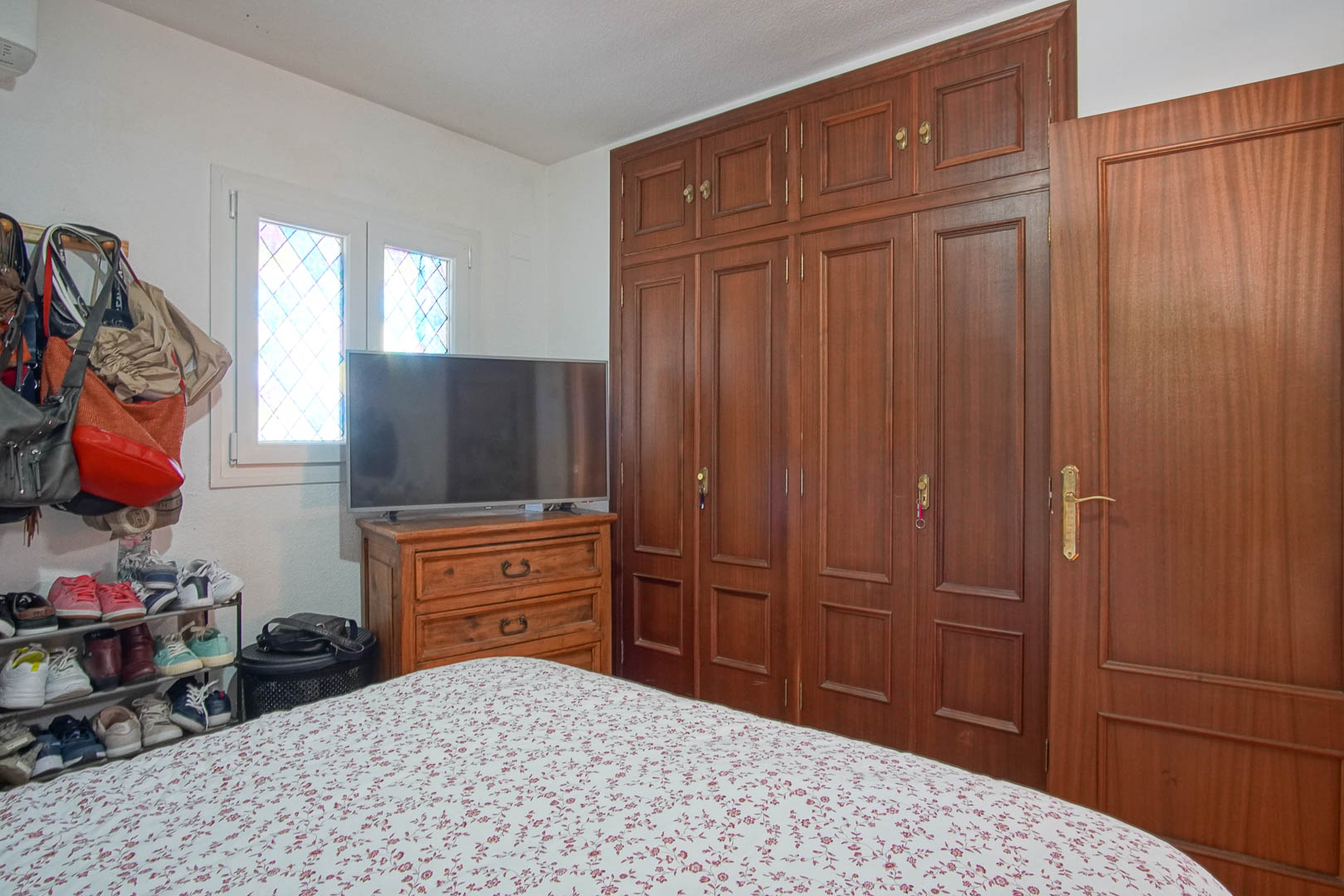 Slaapkamer met een grote kamerhoge houten inbouwkast, bijpassende ladekast met televisie en een raam met glas-in-lood details.