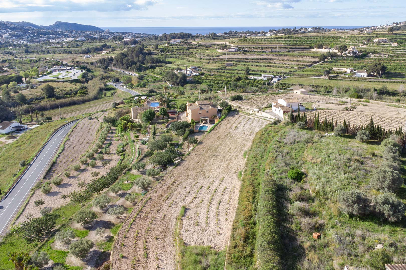 Luchtfoto van het uitgestrekte perceel van 10.920 m2 in Teulada-Moraira, met terrasvormige landbouwgrond en panoramisch uitzicht op de Middellandse Zeekust.