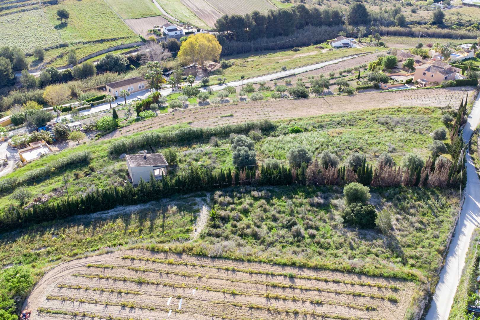 Luchtfoto van het uitgestrekte rustieke perceel in Teulada, met terrasvormig land met mediterrane vegetatie en een bestaand bijgebouw.
