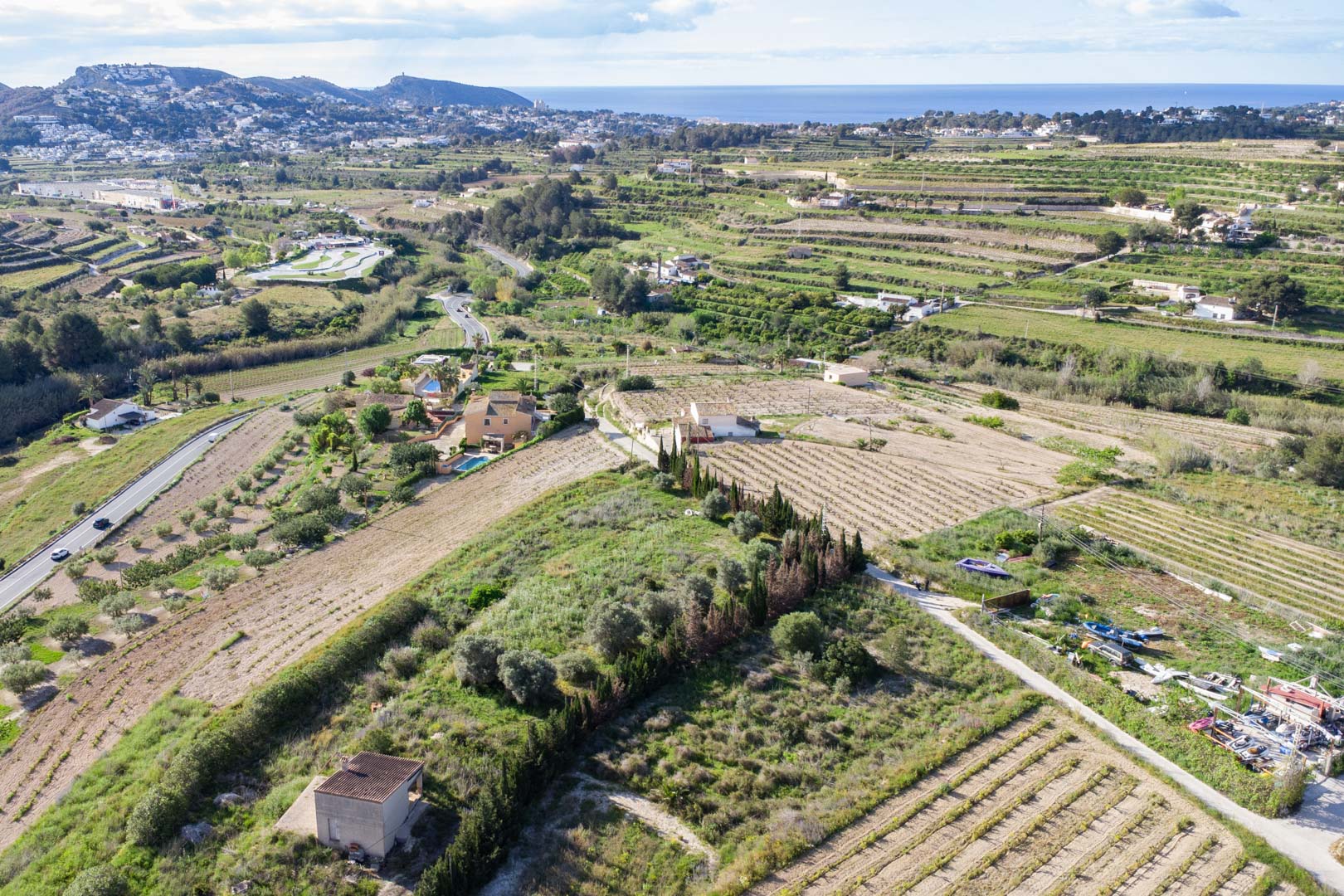 Luchtfoto van het uitgestrekte rustieke perceel van 10.920 m2 in Teulada-Moraira, met terrasvormig terrein en uitzicht op de Middellandse Zee.