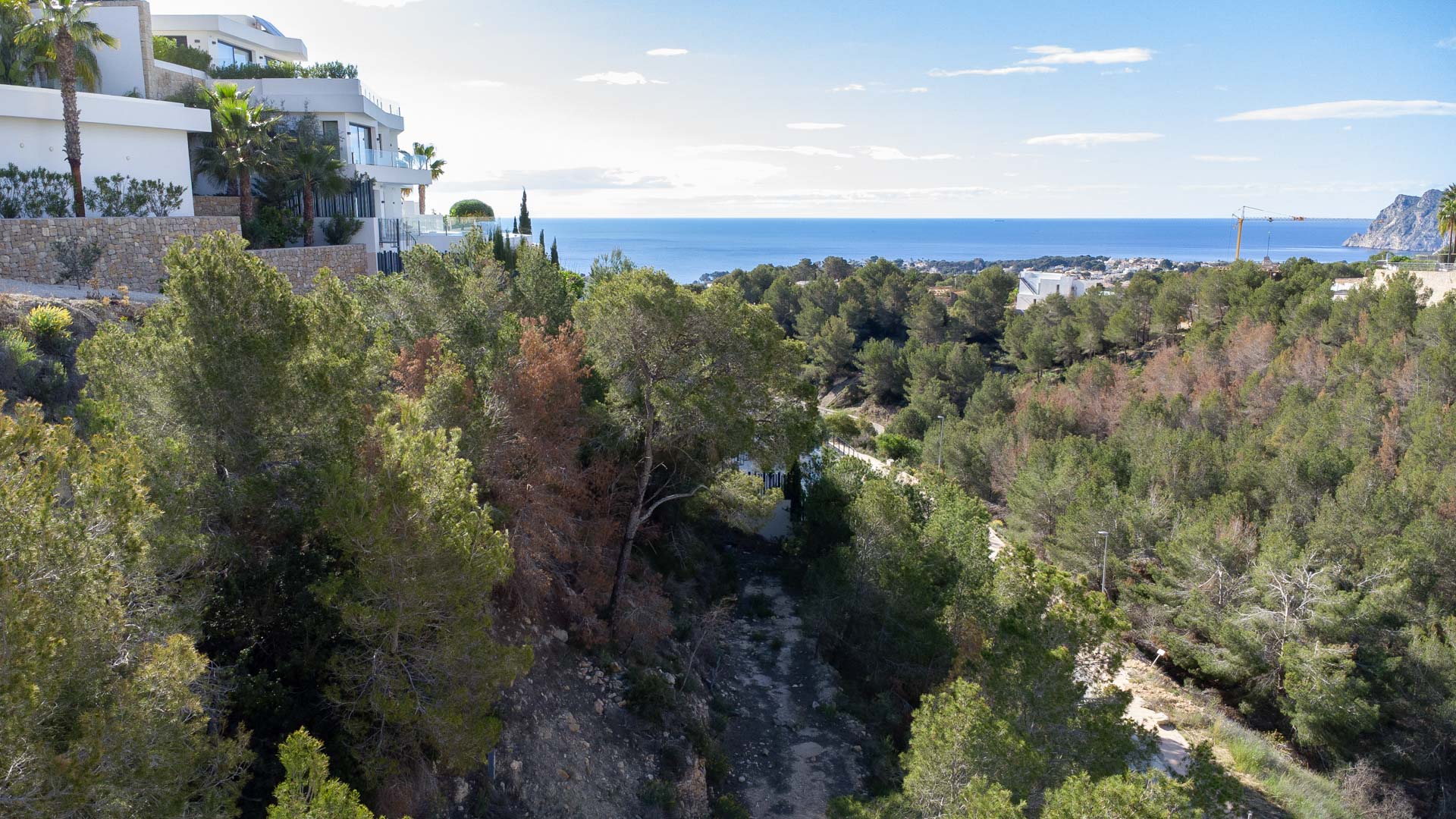 Panoramisch uitzicht op de Middellandse Zee en de Peñón de Ifach vanaf het hoger gelegen perceel, omgeven door pijnbomen en moderne villa's.