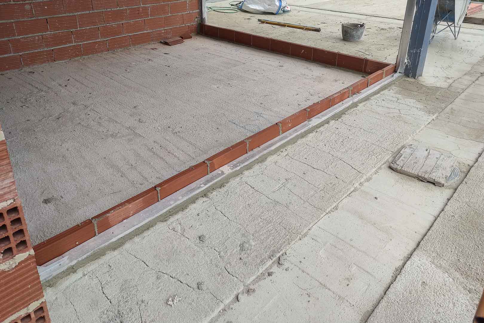 Bouwfase: detail van de vloernivellering en pre-installatie van de metalen profielen voor de grote glazen schuifdeuren van de villa.