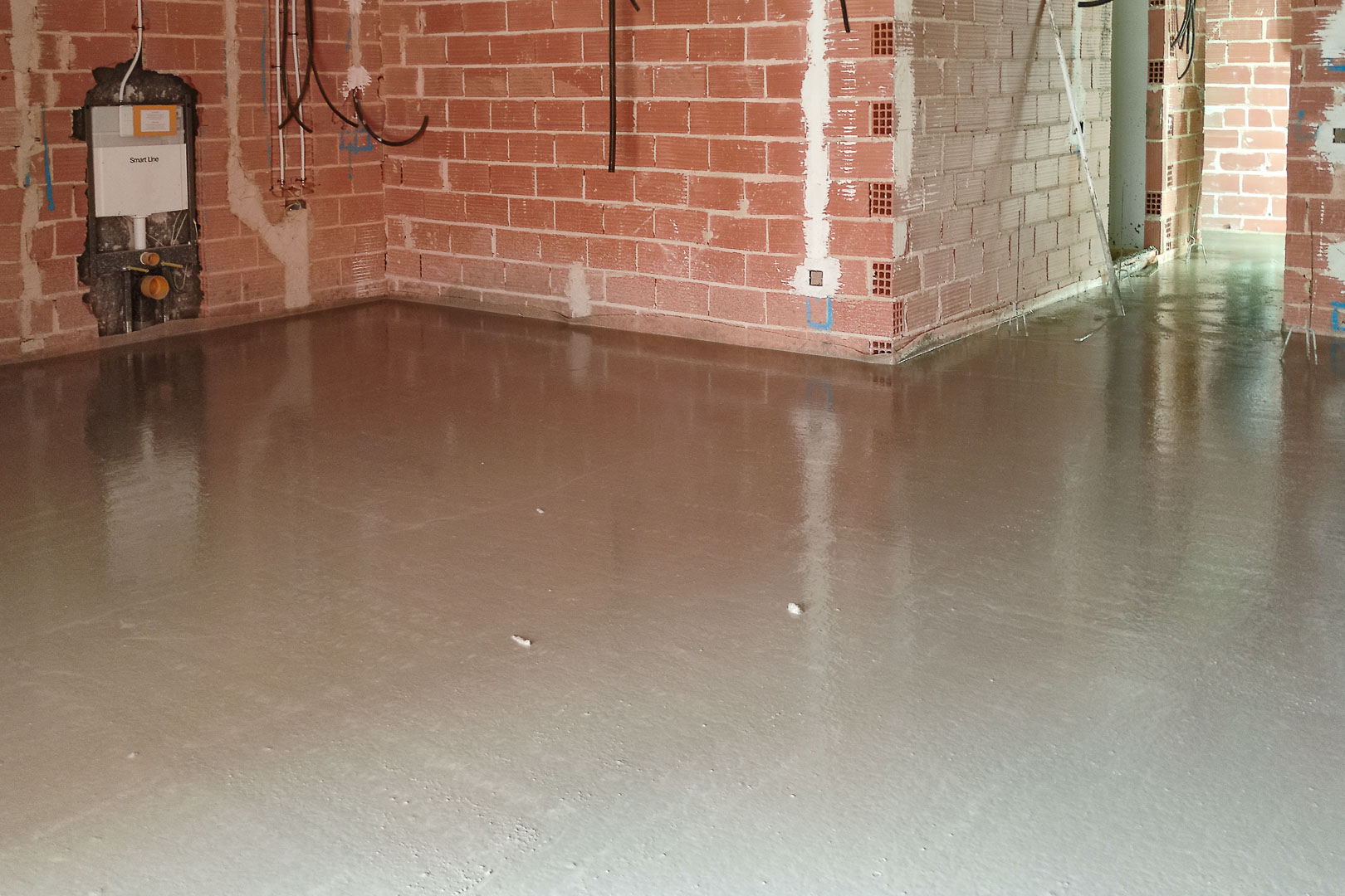 Constructiefase met een vers gegoten zelfnivellerende dekvloer. Zichtbaar metselwerk en installatie van een inbouwreservoir voor een hangend toilet.