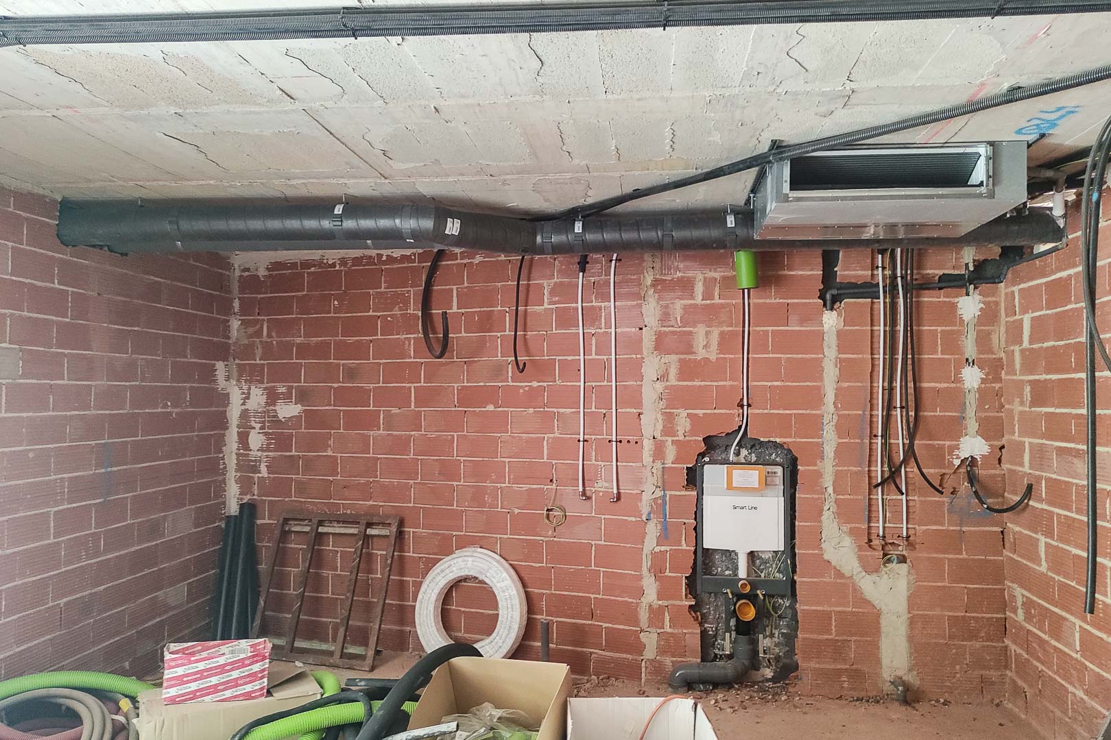 Detail van de ruwbouwfase met de installatie van het aerothermische klimaatsysteem en het inbouwreservoir voor een hangend toilet in de bakstenen muur.