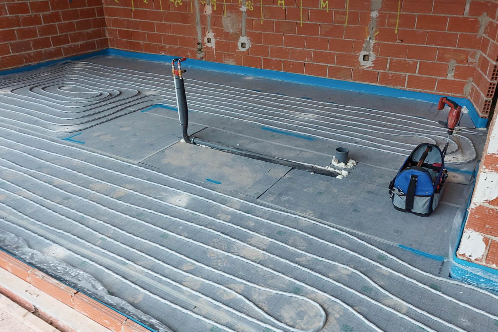 Technische installatie van de vloerverwarming, met de indeling van stralingsbuizen op isolatieplaten in een ruimte tijdens de ruwbouwfase.