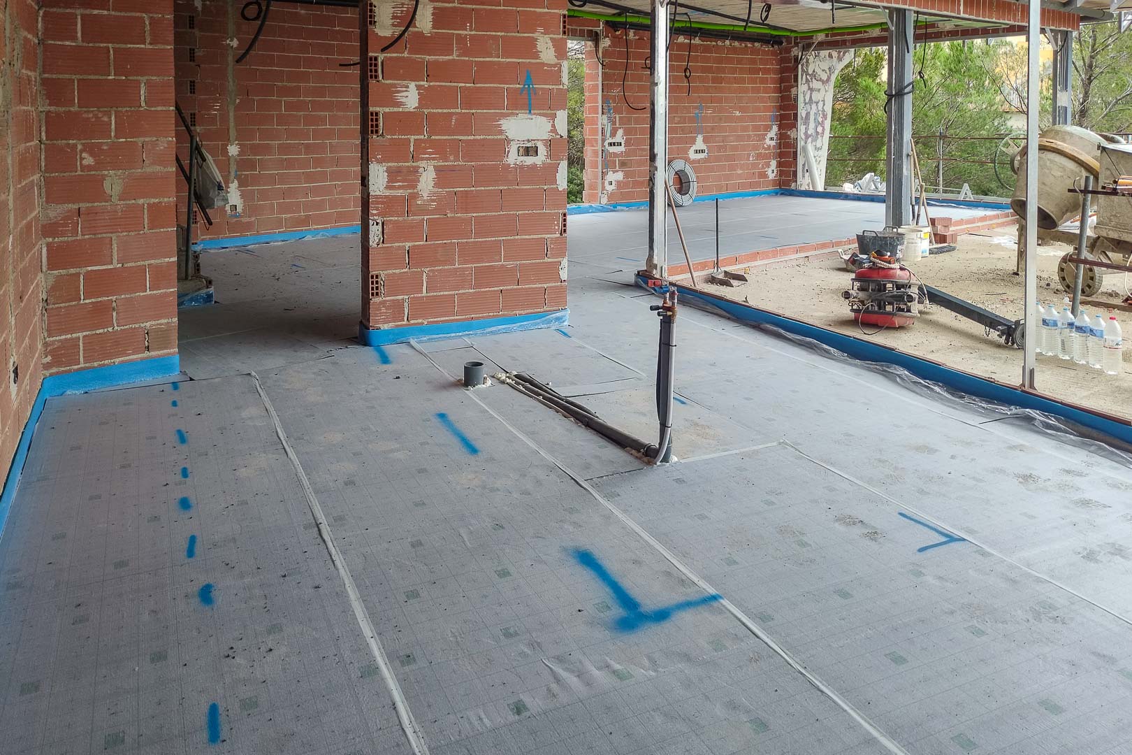 Voortgang van de bouw met vloerisolatiemembraan en leidingwerk ter voorbereiding op de vloerverwarming in de ruwbouw van de villa.
