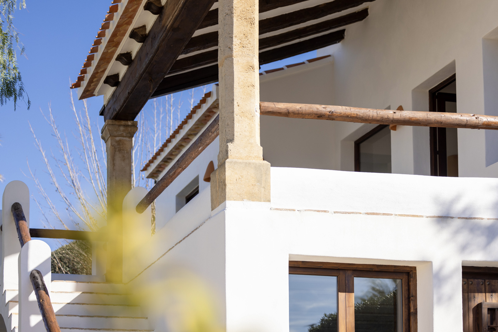 Architectonisch detail van de villa: veranda met houten balken en rustieke balustrade, witte stenen buitentrap.