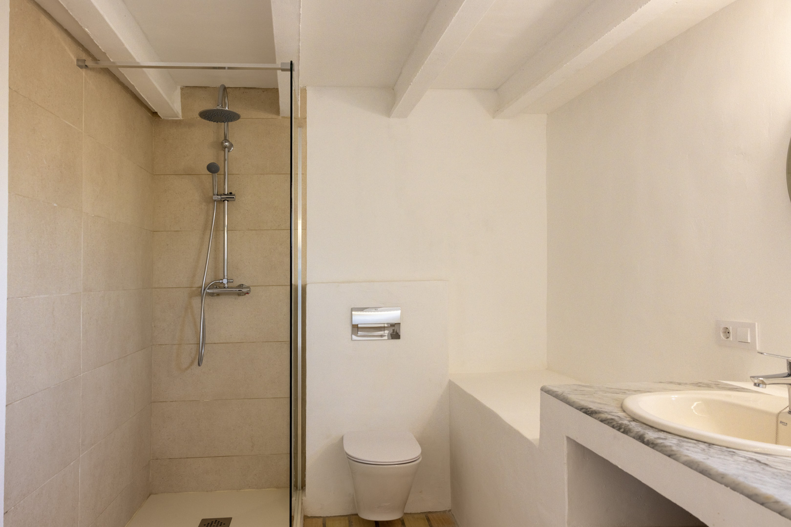 Badkamer met crèmekleurige inloopdouche met tegels, wit toilet en wastafel met marmeren blad.