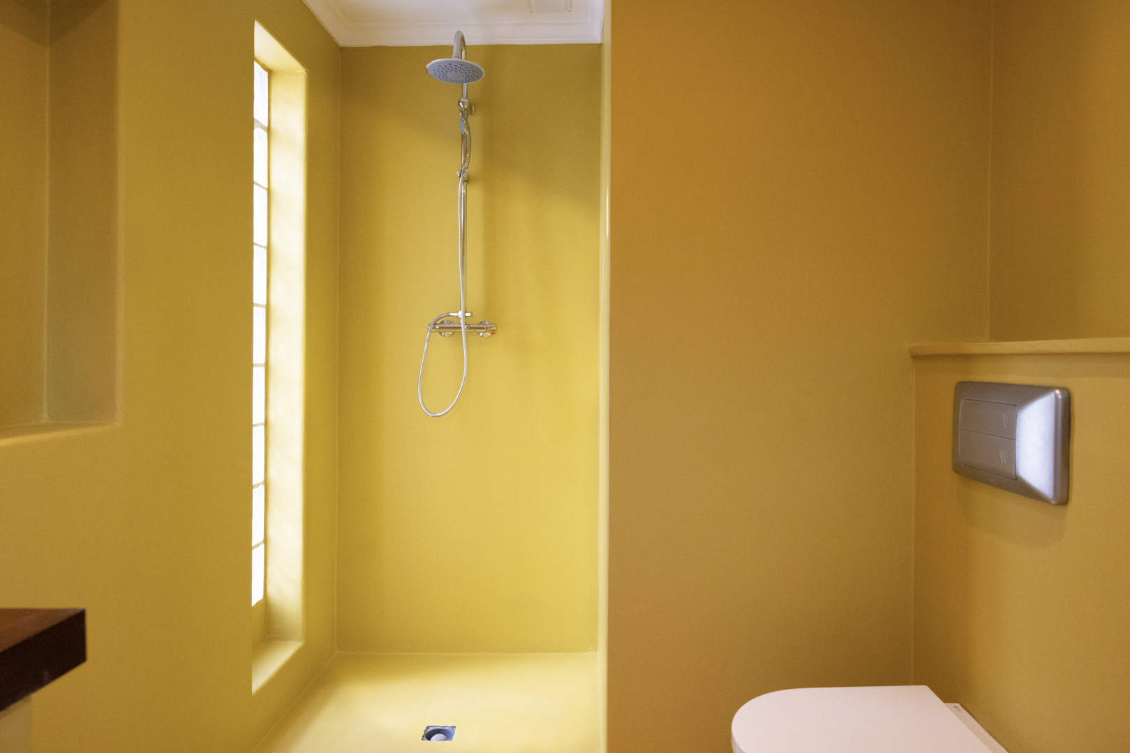 Badkamer met mosterdkleurige muren, stalen douche en verticaal raam.