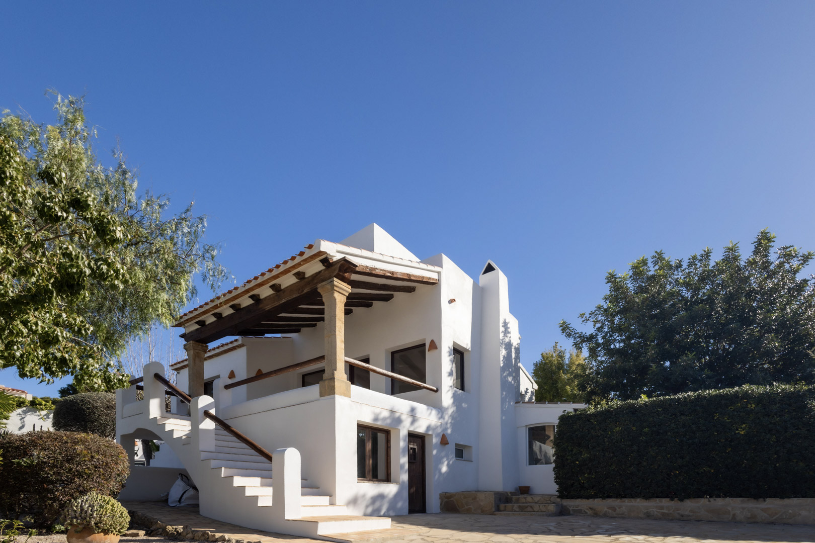 Buitenaanzicht van de gerenoveerde villa, met de nadruk op de traditionele Spaanse architectuur en het overdekte terras met houten balken.
