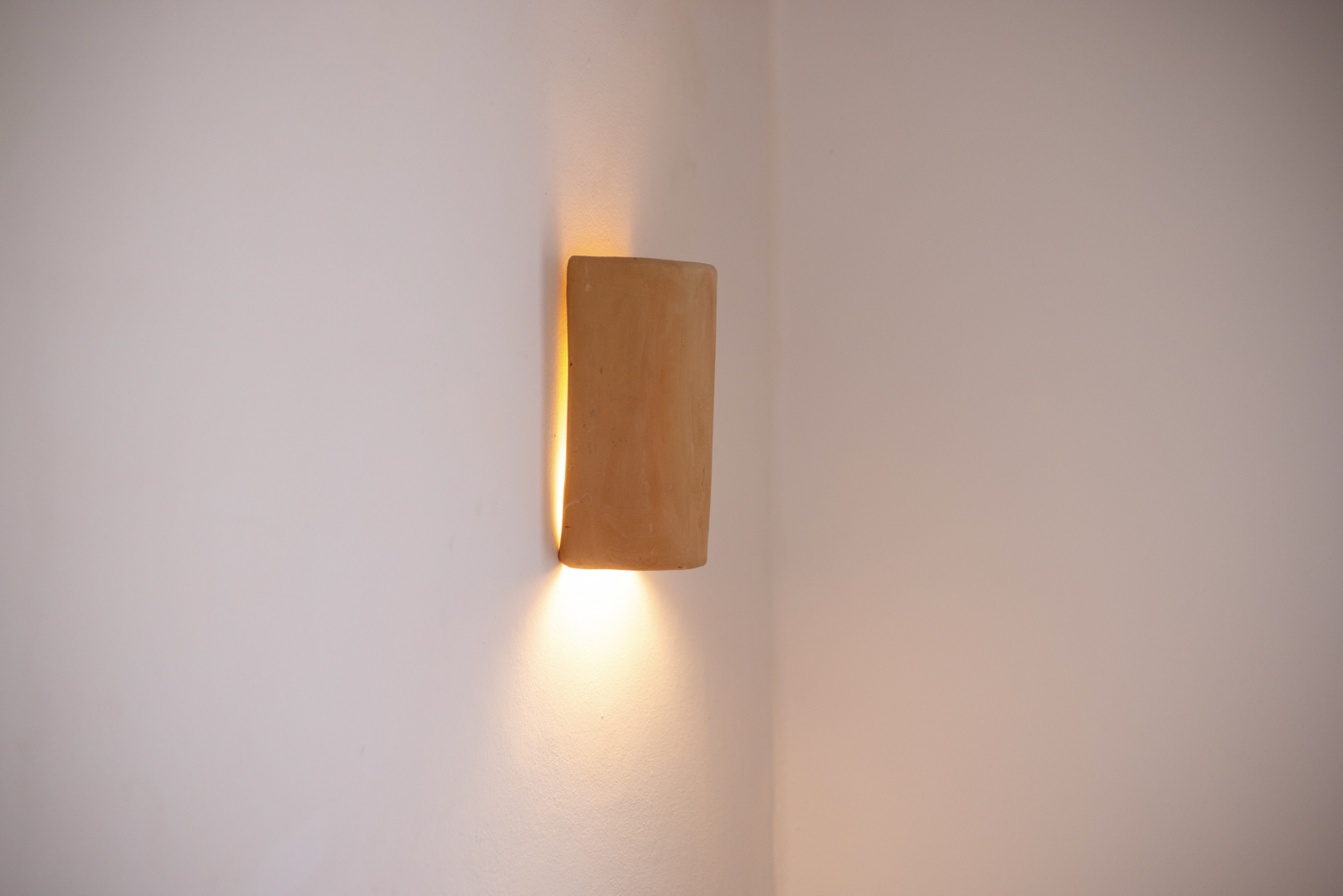 Detail van een rustieke wandlamp, die een warme gloed verspreidt in een minimalistisch interieur.