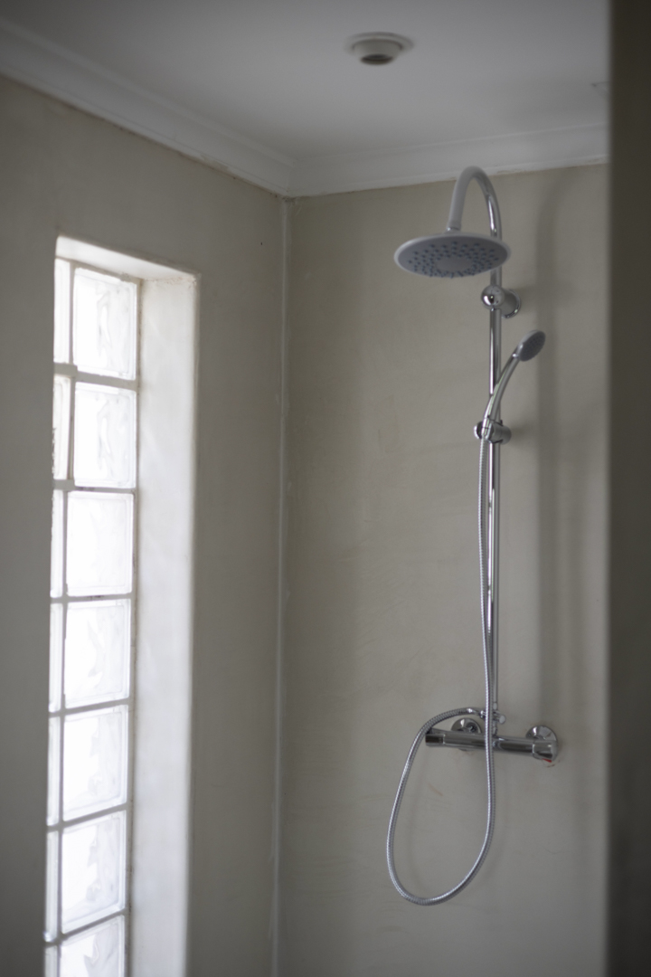 Douche detail met regendouchekop en glazen bouwsteenvenster in een badkamer met crèmekleurige muren.